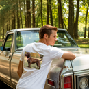The image of a Wear-it-around collection of 't-shirts' featuring a young man leaning on the hood of an old 1970 car. The man is in a white t-shirt with a patriotic Labrador Retriever design.